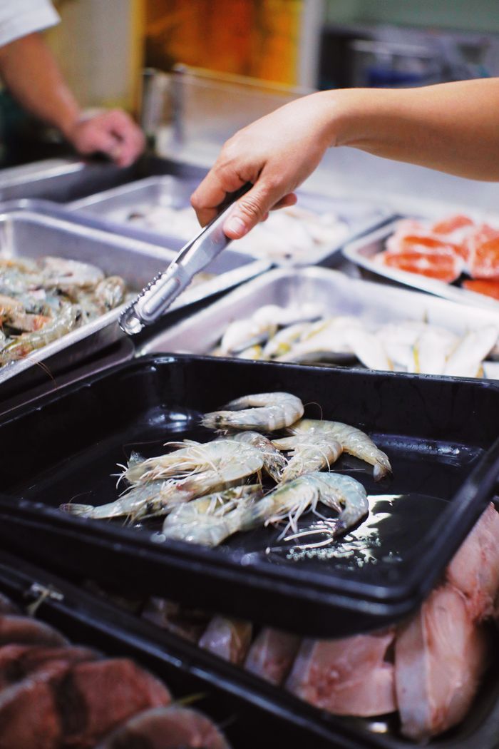 Crop unrecognizable seller using metal tongs for taking fresh shrimps in local market in daytime